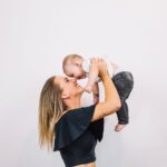 Photo of a mother wearing a black top holding her child up, wondering "What is a Mommy Makeover?"