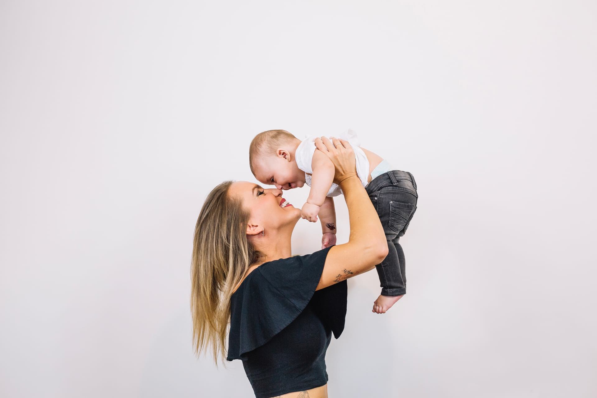 Photo of a mother wearing a black top holding her child up, wondering "What is a Mommy Makeover?"