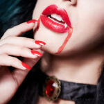 Cose-up of young beautiful woman's face dressed for Halloween and wearing vampire fangs.