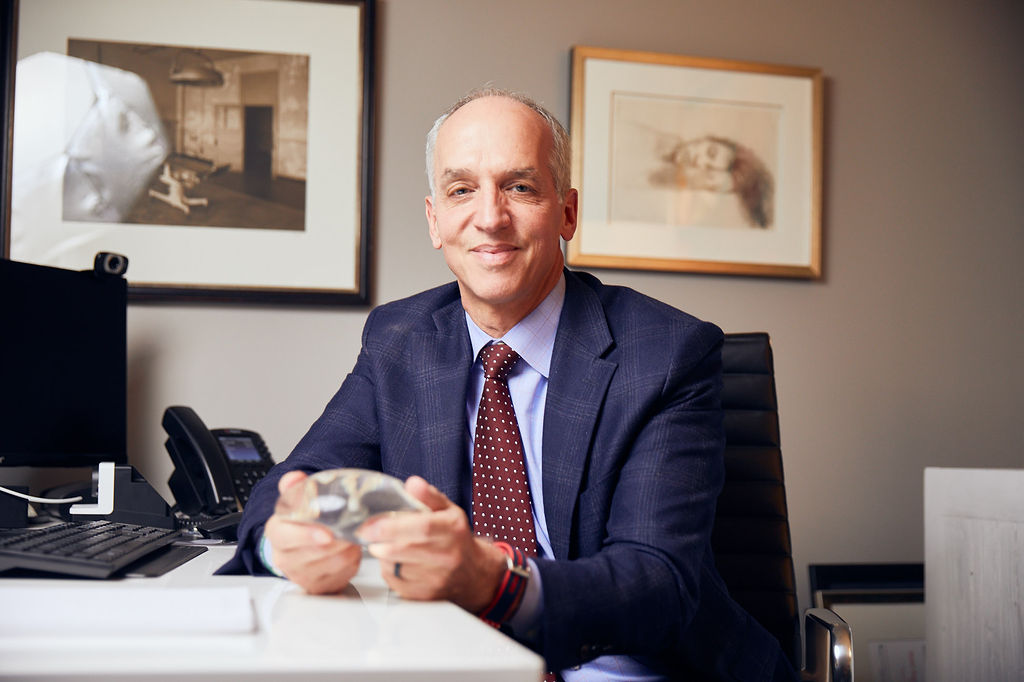 Dr. Peter Capizzi board certified plastic surgeon sitting with breast implant in hand
