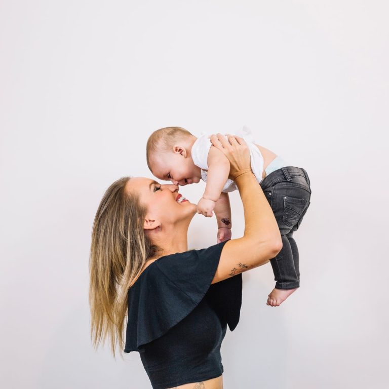 Photo of a mother wearing a black top holding her child up, wondering "What is a Mommy Makeover?"